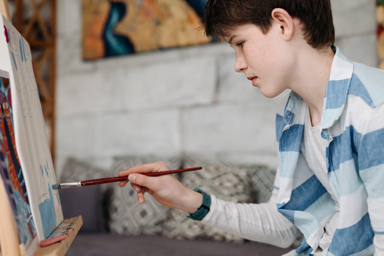 A young boy attentively painting on a canvas, embracing creativity and imagination in art.