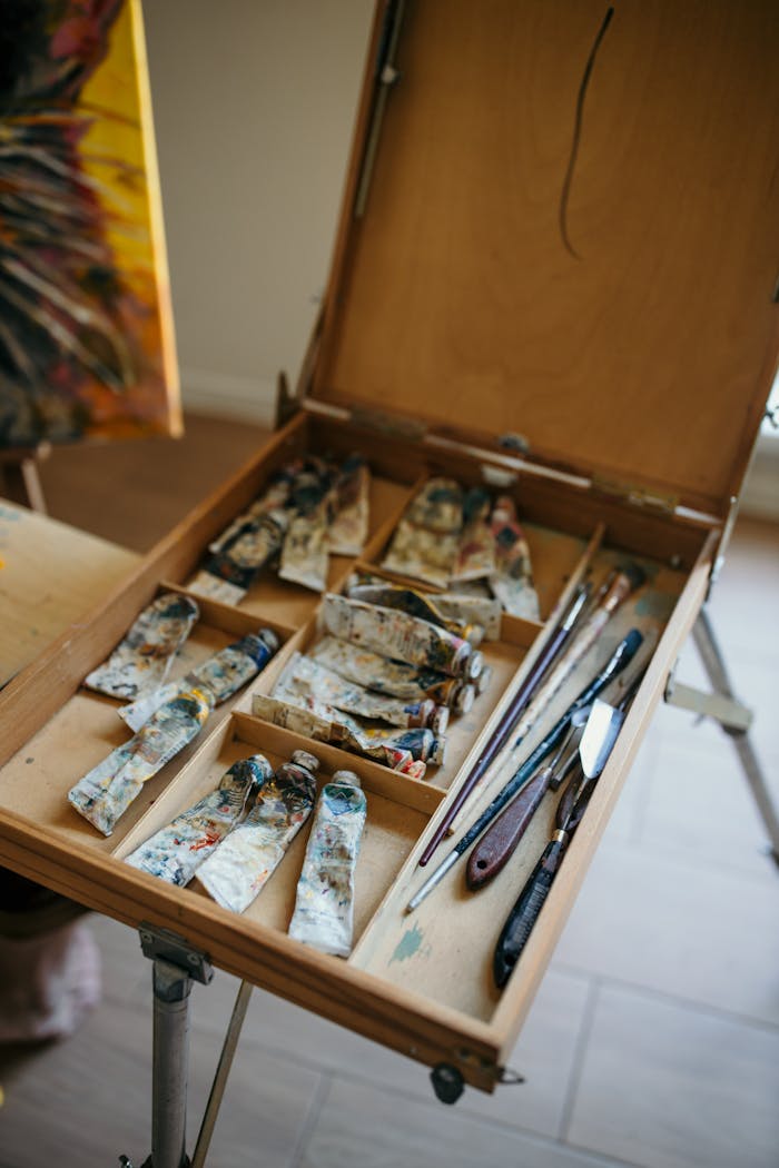 Wooden artists box with paints and brushes on an easel, indoors.