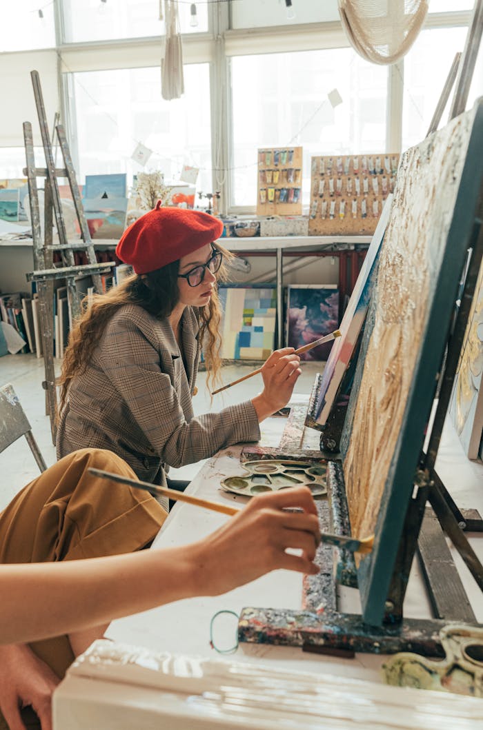 Young woman in beret painting on canvas in a light-filled art studio, capturing creativity.